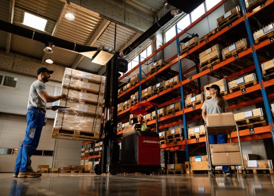 Below view of group of workers cooperating in a warehouse. Low angle view of happy warehouse workers communicating while working with shipment in industrial storage compartment.